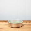 Empty gold pet bowl on a wooden floor with a white wall background.