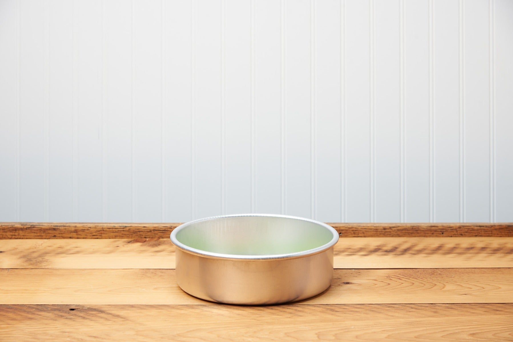 Empty gold pet bowl on a wooden floor with a white wall background.