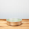 Empty gold-colored cake pan on wooden countertop with light backdrop