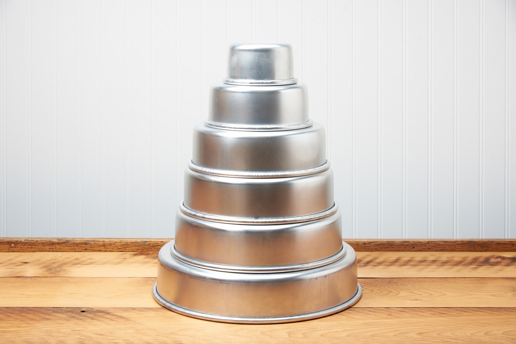 Silver tiered round cake stand on a wooden table against a white beadboard background