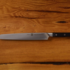 Stainless steel serrated bread knife with black handle on wooden surface