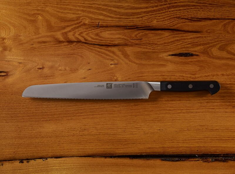 Stainless steel serrated bread knife with black handle on wooden surface