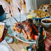Person carving roasted chicken on festive table with dog watching in background