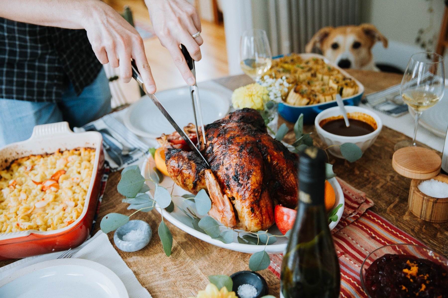 Person carving roasted chicken on festive table with dog watching in background