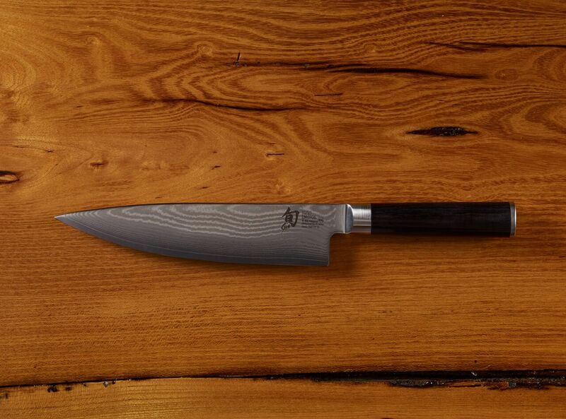 Damascus steel chef knife with black handle on wooden background