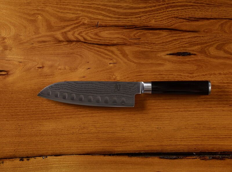Damascus chef knife with black handle on wooden background