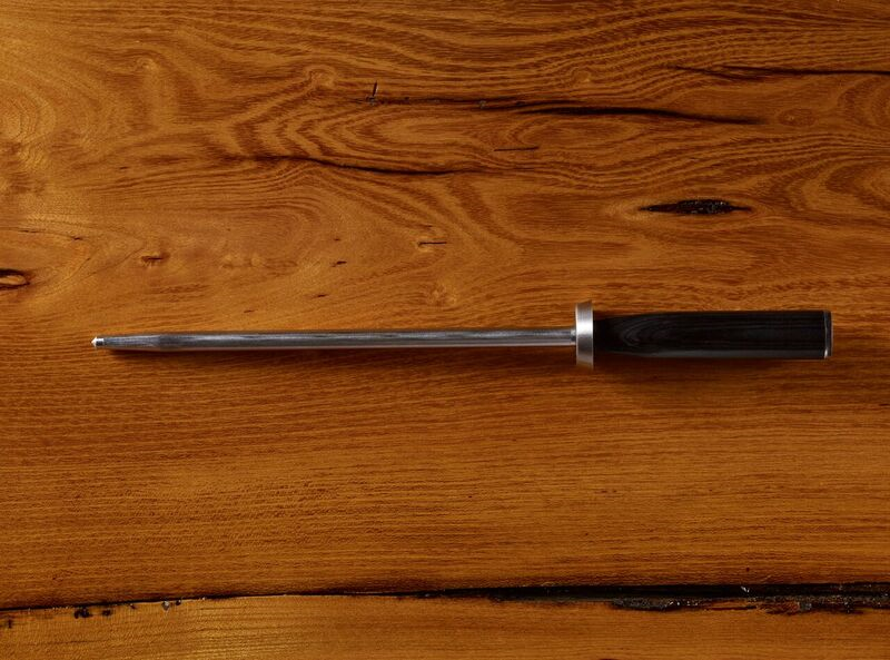 Stainless steel honing rod with black handle on wooden background