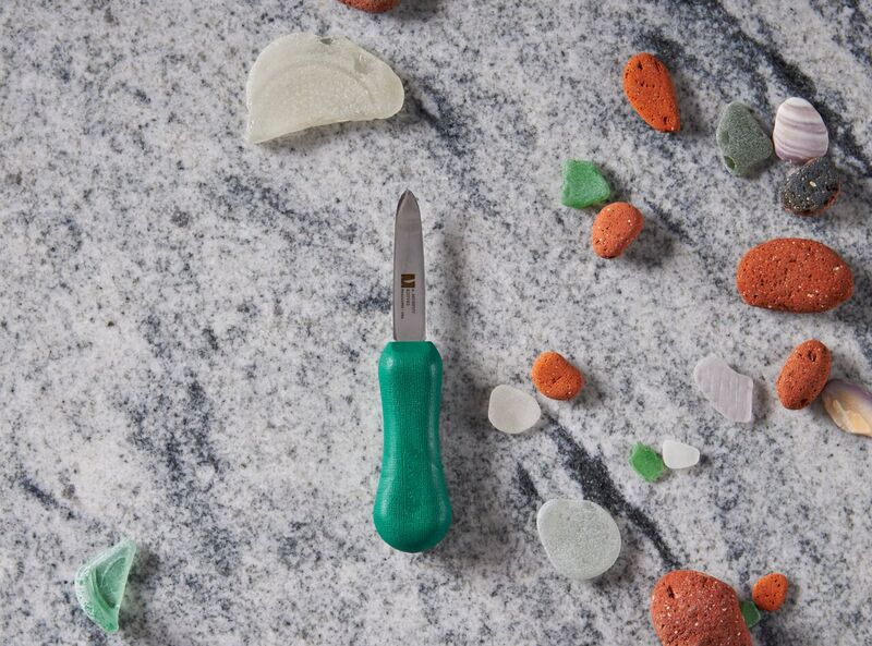 Green-handled knife on marble surface surrounded by colorful sea pebbles.