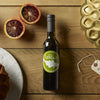 Stylish bottle of Leroux olive oil, blood oranges, and bundt cake pan on wooden table.