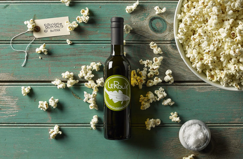 Bottle of LeRoux olive oil with popcorn and sea salt on wooden table.