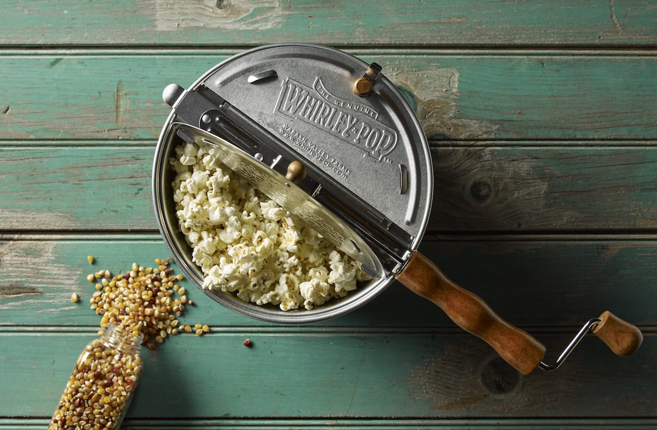 Vintage popcorn maker filled with popcorn on a rustic wooden surface