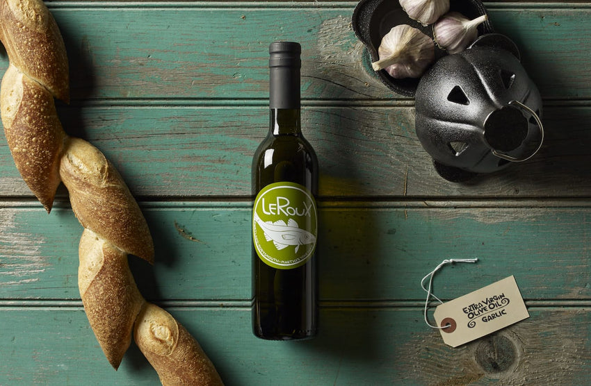 Rustic kitchen setting with a bottle of LeRoux wine, fresh baguettes, garlic, and garlic press.