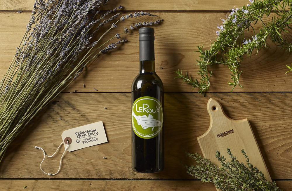 Bottle of LeRoux olive oil with herbs and lavender on wooden table.