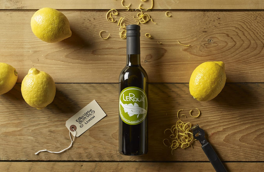 Bottle of LeRoux lemon olive oil with fresh lemons and zest on wooden table