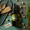 Olive oil bottle with label, fresh baguettes, wooden utensils, and grill pan on teal background.