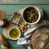 Rustic bread with olive oil, olives, sardines, and sea salt on worn wooden table.