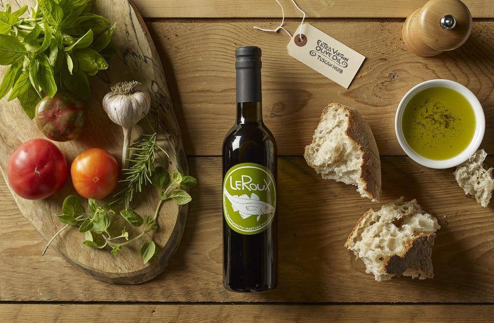 Olive oil bottle with fresh herbs, tomatoes, garlic, and bread on wooden table