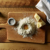 Ingredients for pasta dough on wooden board with flour well and egg