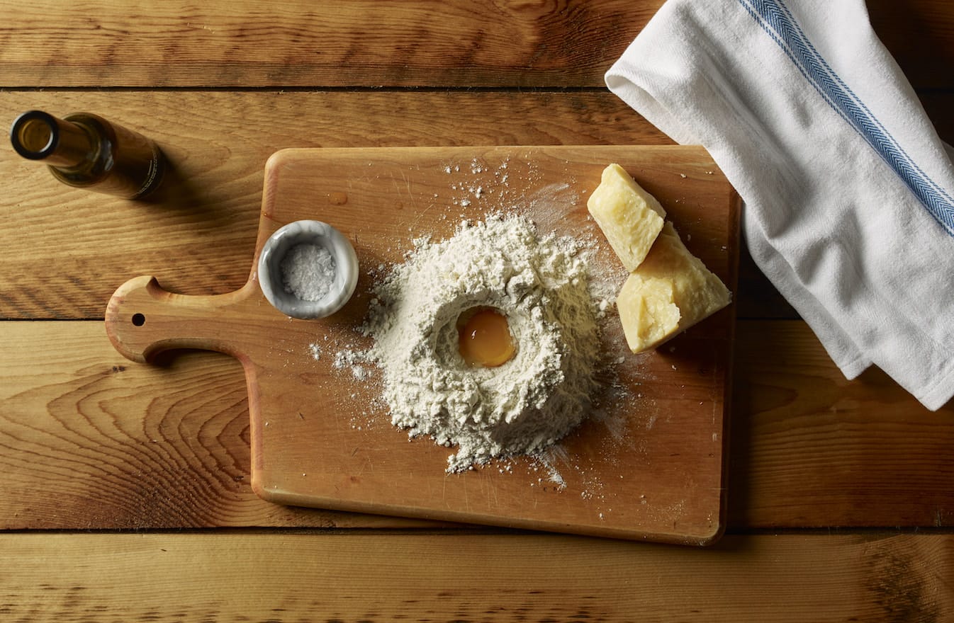 Ingredients for pasta dough on wooden board with flour well and egg