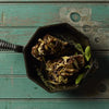 Cast iron skillet with roasted meat and herbs on teal wooden background