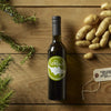 Extra virgin olive oil bottle with rosemary sprigs, potatoes, and salt on wooden table.