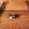 Wine bottle with open cork and two wine pourer stoppers on wooden surface.