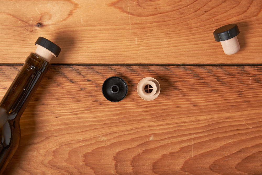 Brown glass bottle with stopper and two small button-like items on wood surface