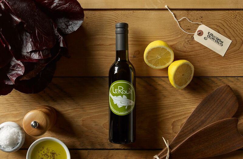 Olive oil bottle on wooden table with lemons, salt, and fresh greens
