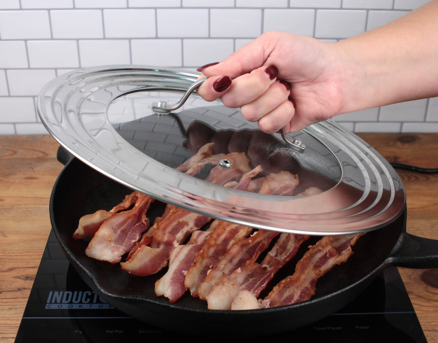 An RSVP Universal Glass Lid 7”-12” is used to cover a cast iron skillet full of bacon.