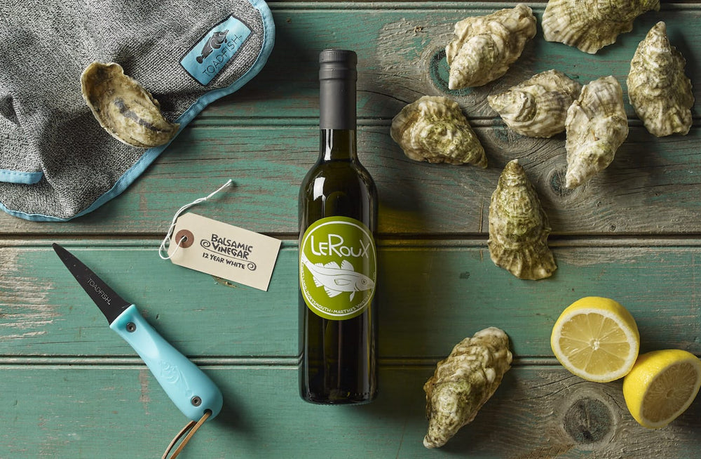 Bottle of white wine, oysters, lemon slices, and shucking knife on wooden table