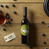 Bottle of LeRoux vinegar with blueberry tag, honey jar, fresh blueberries, and waffle iron on wooden table.