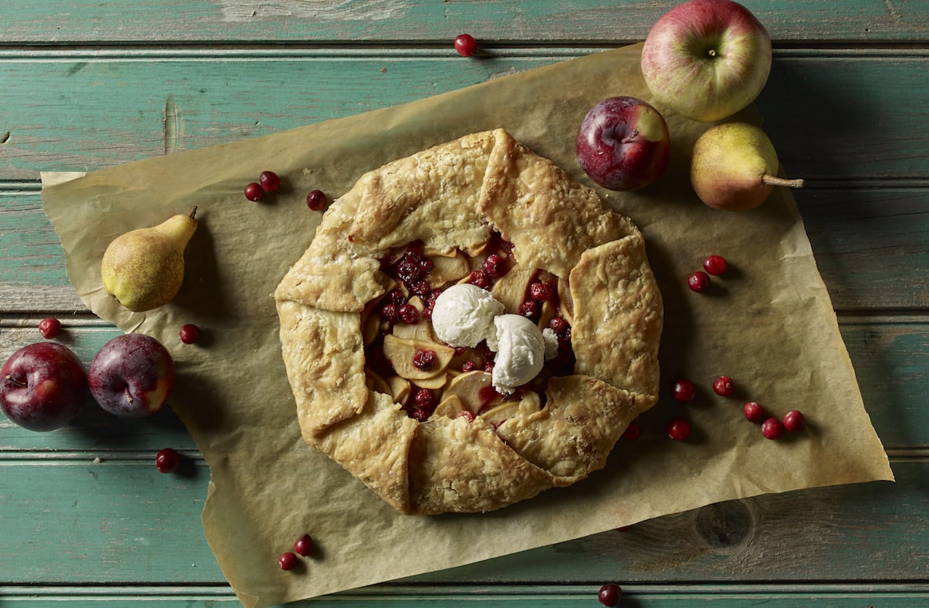 Rustic apple cranberry pie with scoop of vanilla ice cream, fresh fruits on wooden surface