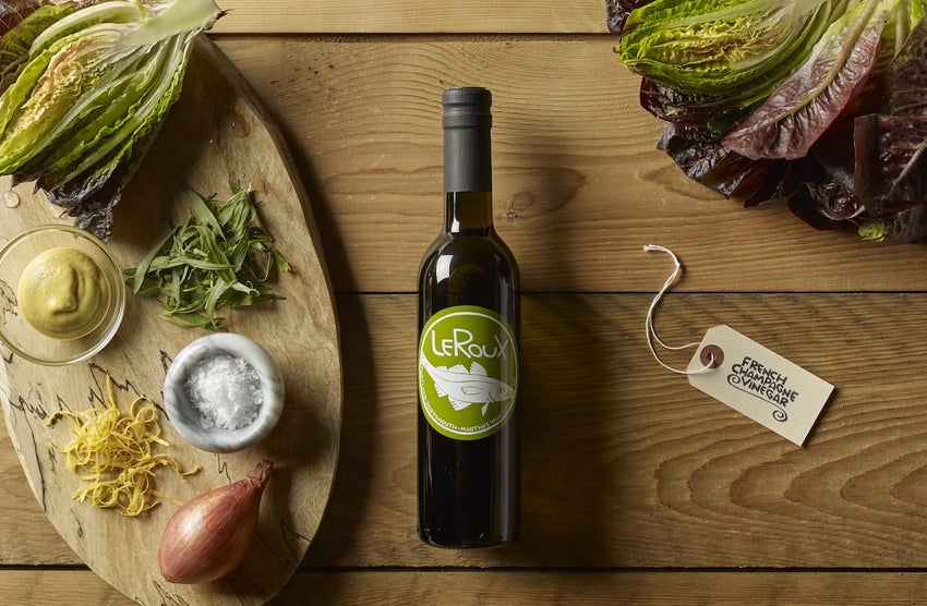 Olive oil bottle on wooden board with fresh greens, shallot, lemon zest, and sea salt.