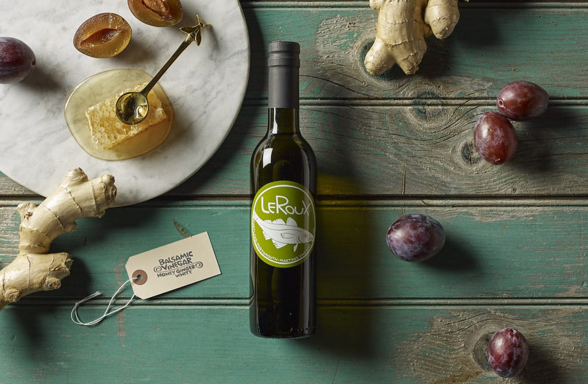 Gourmet bottle of olive oil, honey on marble, plums, and ginger on wooden table.