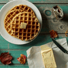 Waffles with butter on plate, maple syrup, autumn leaves on rustic wood table