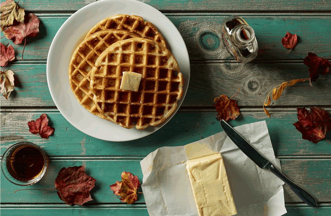 Waffles with butter on plate, maple syrup, autumn leaves on rustic wood table