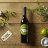 Organic olive oil bottle with herbs, garlic, tomato, and sea salt on wooden table.