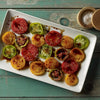 Assorted sliced heirloom tomatoes with balsamic drizzle on a white plate, wooden table background.
