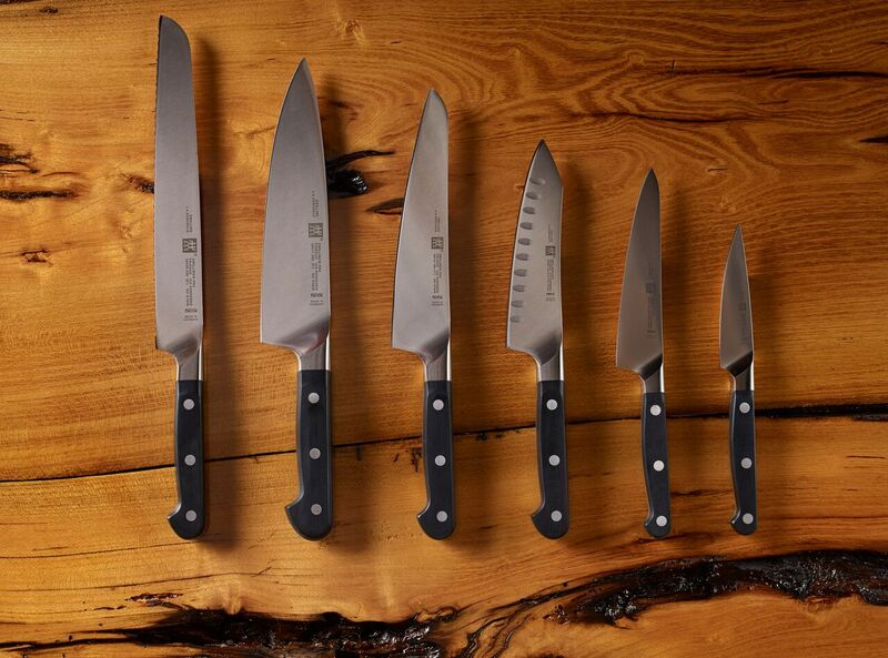 Set of six chef knives arranged in ascending size on a wooden background